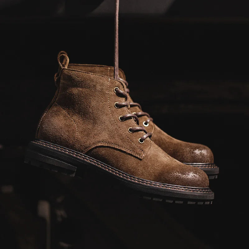 Brown suede lace-up ankle boots for men with rugged sole hanging against dark background