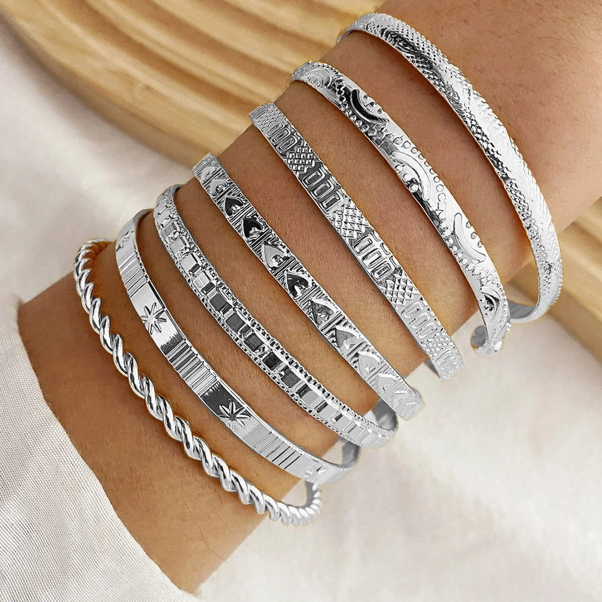 Six silver etched bangle bracelets stacked on wrist, featuring twisted rope, geometric, and floral engraved designs