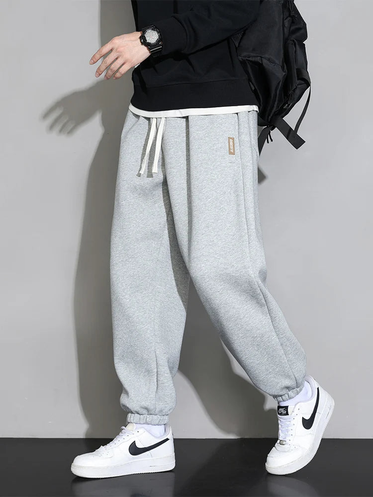 Men's gray cotton joggers with elastic cuffs, white drawstring waist, relaxed fit sweatpants worn with black hoodie