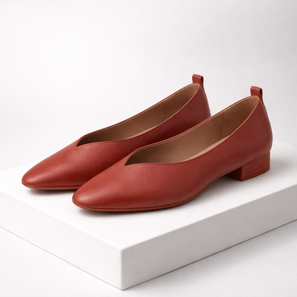 Rust red Italian leather pointed-toe pumps with V-cut vamp, block heel, and tan interior on white display stand.