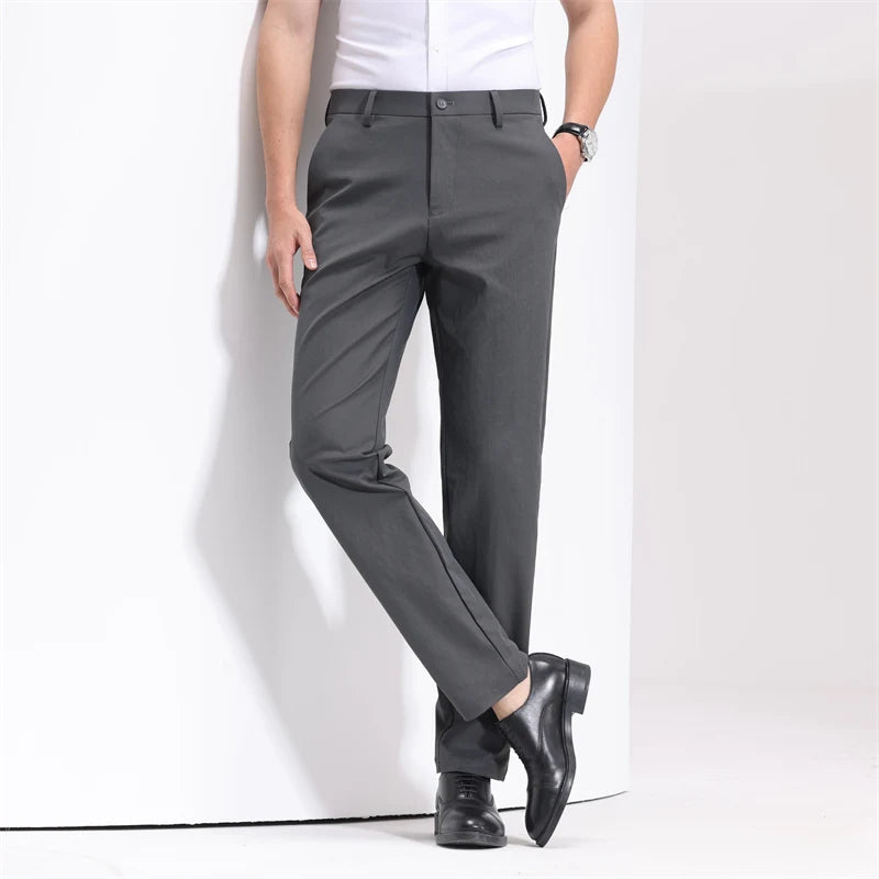 Man wearing slim-fit gray cotton dress trousers with black leather shoes and white shirt, leaning against white wall