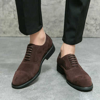 Brown suede cap-toe Oxford dress shoes with lace-up closure, paired with black dress pants on a gray background.