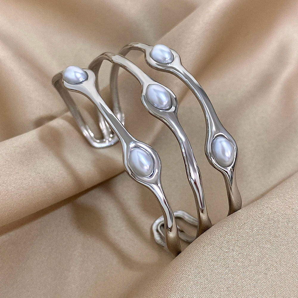 Silver tone open cuff bangles with embedded oval freshwater pearls displayed on beige satin fabric