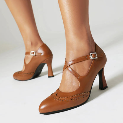 Tan leather block heel pumps with cross-ankle straps, silver buckle, and brogue wingtip detailing on pointed toe.
