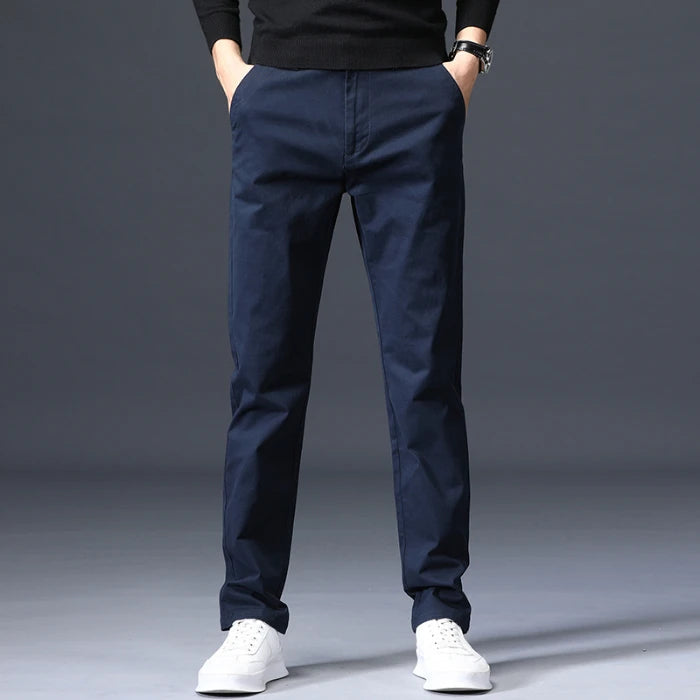Navy blue slim-fit men's cotton dress pants worn with white sneakers and black sweater, straight leg style.