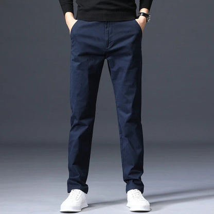 Navy blue slim-fit men's cotton dress pants worn with white sneakers and black sweater, straight leg style.