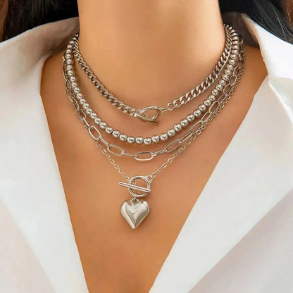 Silver layered chain necklace set with heart pendant, bead strand, curb chain, and toggle clasps on woman in white top