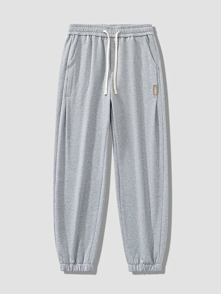 Light gray men's relaxed fit cotton jogger pants with white drawstring waistband, side pockets, and elastic cuffed ankles.