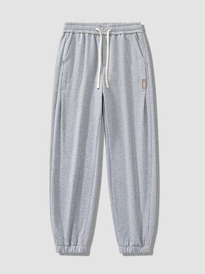 Light gray men's relaxed fit cotton jogger pants with white drawstring waistband, side pockets, and elastic cuffed ankles.