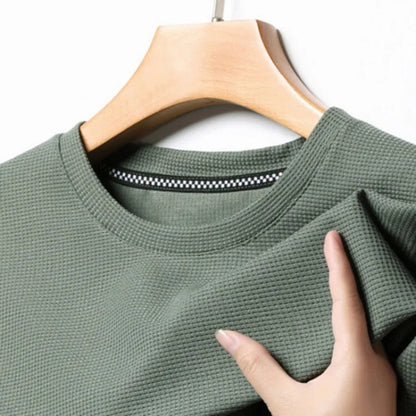 Army green men's waffle knit crewneck t-shirt on wooden hanger, showing textured fabric detail and inner neck tape.