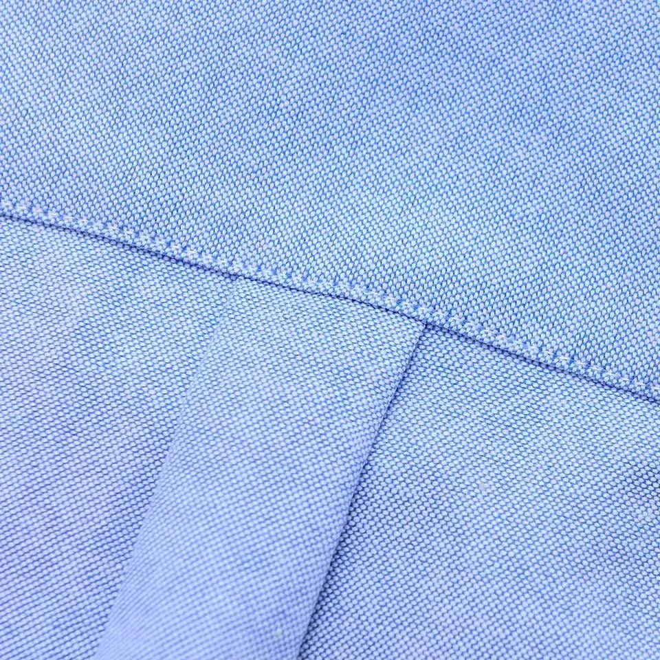 Close-up of light blue oxford cotton fabric showing fine weave texture and neat stitched seam detail on men's button-down shirt