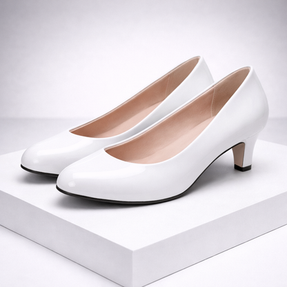 White patent leather kitten heel pumps with round toe and blush pink interior, displayed on white platform
