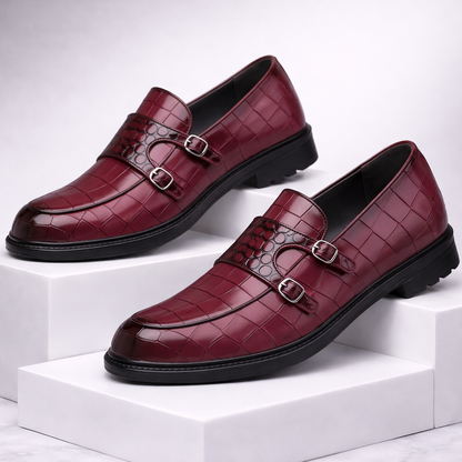 Burgundy croc-embossed leather double monk strap loafers with silver buckles and black chunky sole displayed on white blocks