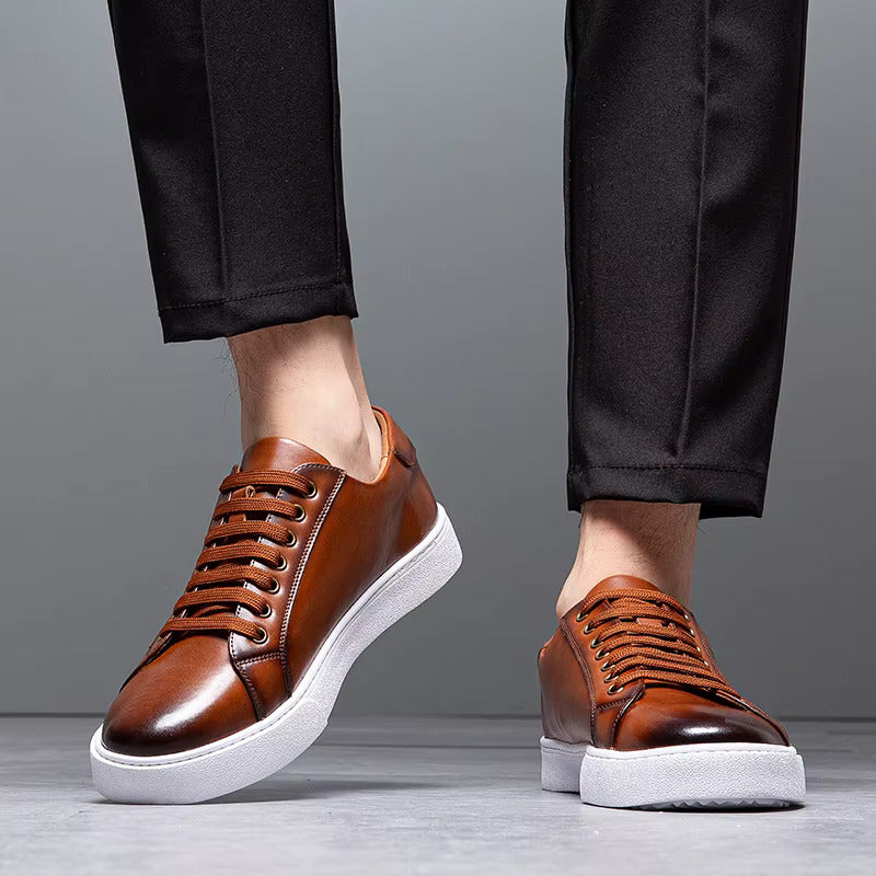 Men's brown leather lace-up sneakers with white sole, paired with black dress pants, shown from ankles down.