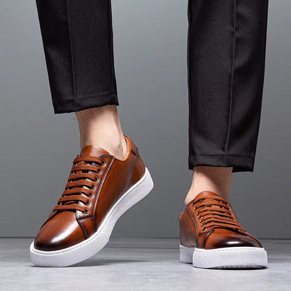 Men's brown leather lace-up sneakers with white sole, paired with black dress pants, shown from ankles down.