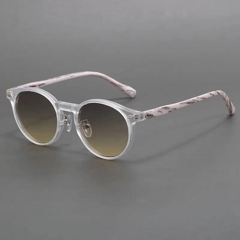Round sunglasses with clear frames, patterned pink temples, and gradient brown lenses on gray background