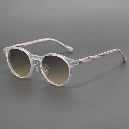 Round sunglasses with clear frames, patterned pink temples, and gradient brown lenses on gray background