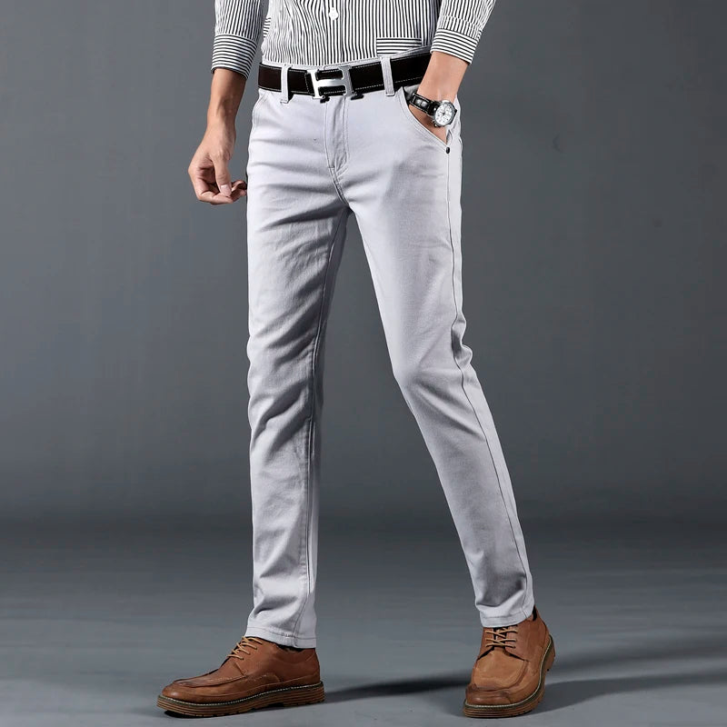 Men's slim-fit light gray cotton dress pants with black belt, paired with striped shirt and brown leather shoes.