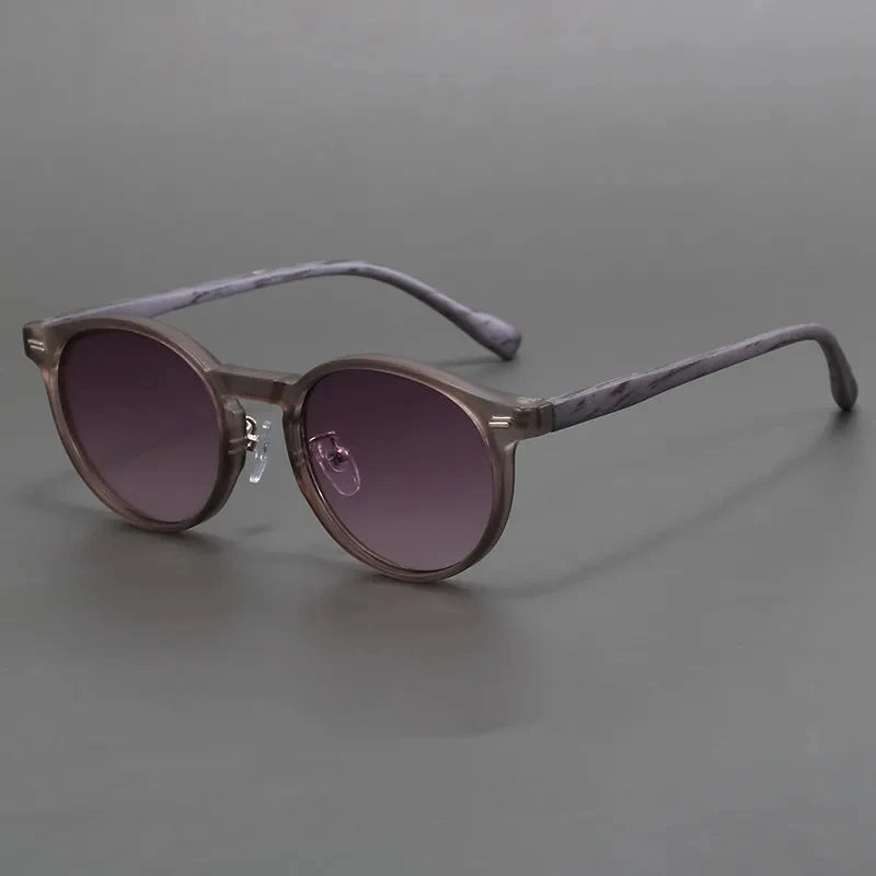 Round gray tortoiseshell acetate sunglasses with gradient purple-brown lenses and marbled temple arms on gray background