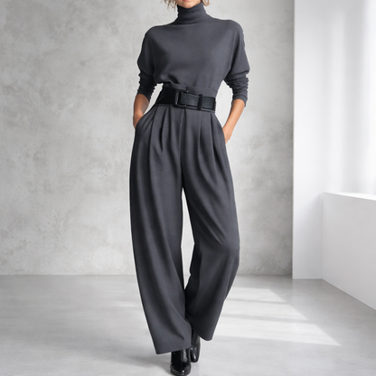 Women's charcoal gray turtleneck top and wide-leg pleated pants set with black belt and black ankle boots.