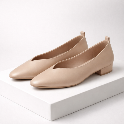 Nude beige leather pointed-toe block heel pumps with V-cut vamp and small stacked heel on white display platform
