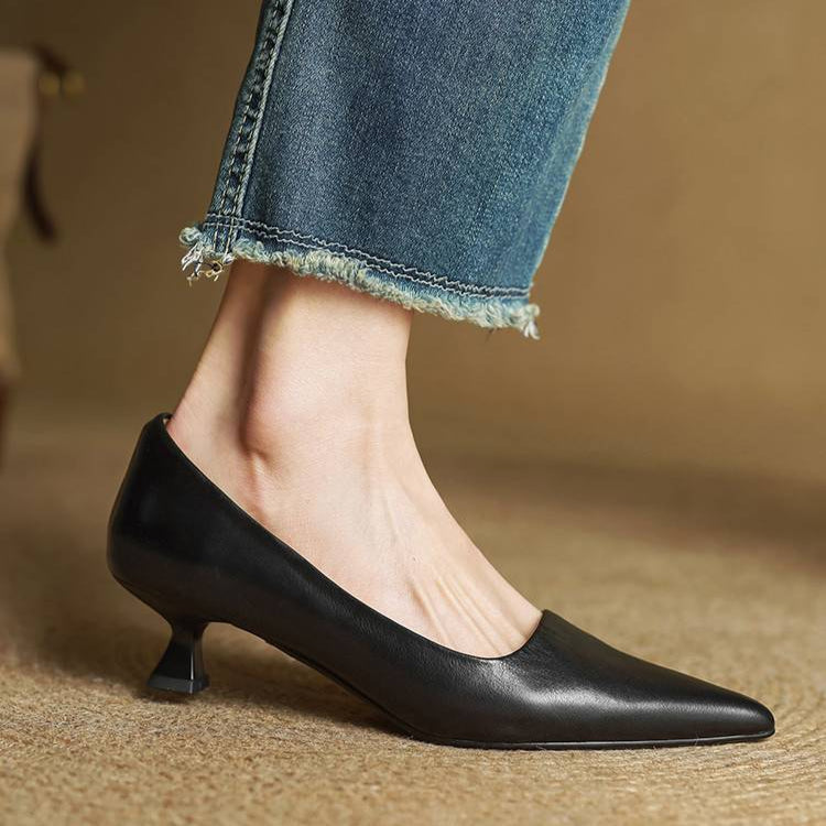 Women's black leather pointed-toe pumps with kitten heel, styled with cropped frayed denim jeans on woven floor.