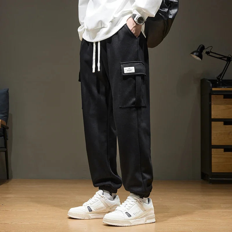 Black men's cargo jogger pants with drawstring waist, side pocket label detail, paired with white sneakers