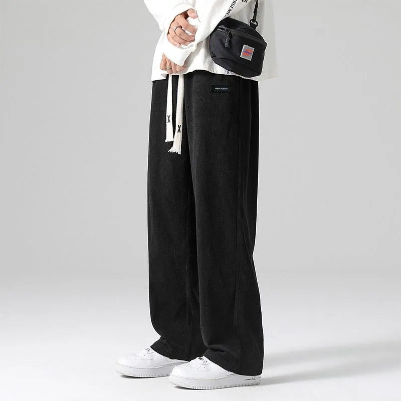Black corduroy wide-leg sweatpants with drawstring waist, worn with white sneakers and casual streetwear outfit.
