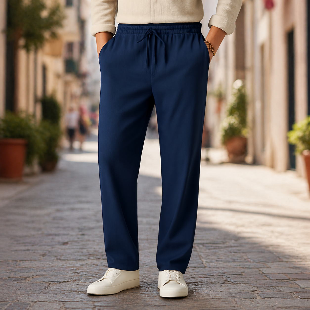 Navy blue men's linen drawstring casual pants with elastic waist, side pockets, worn with white sneakers on cobblestone street.