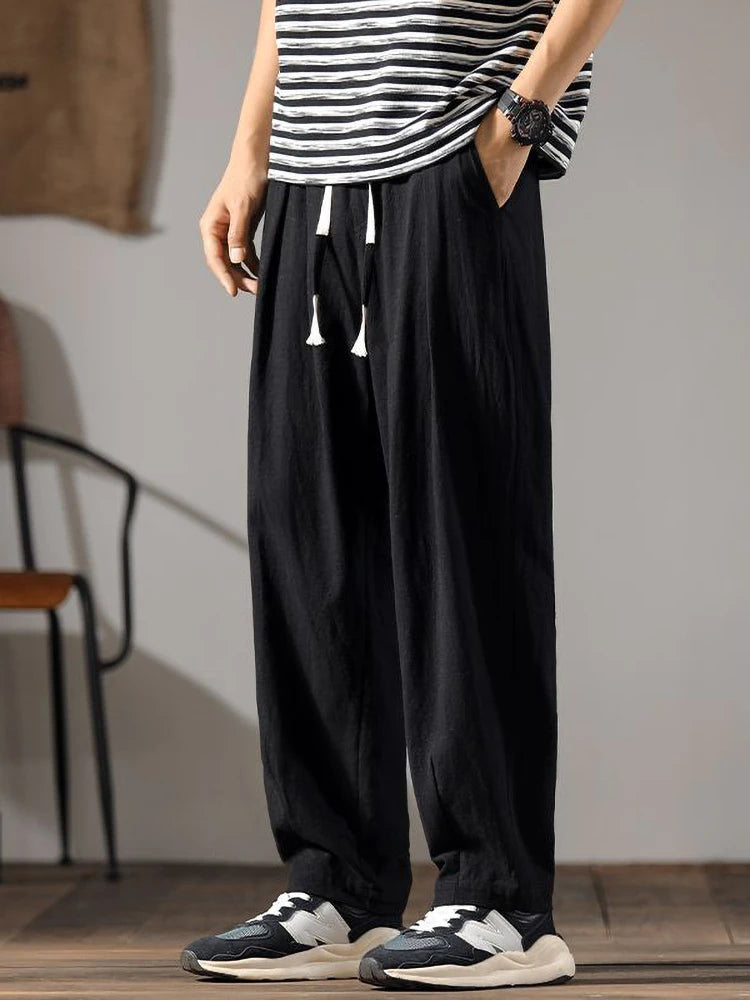 Men's black wide-leg drawstring linen pants paired with striped tee and sneakers, shown from waist to ankle.