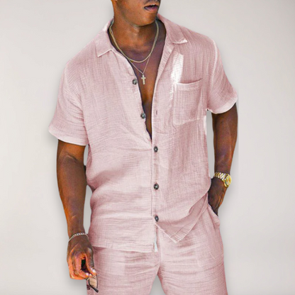 Man wearing a pink linen short-sleeve button-up shirt and matching pants set with chest pocket and dark buttons.