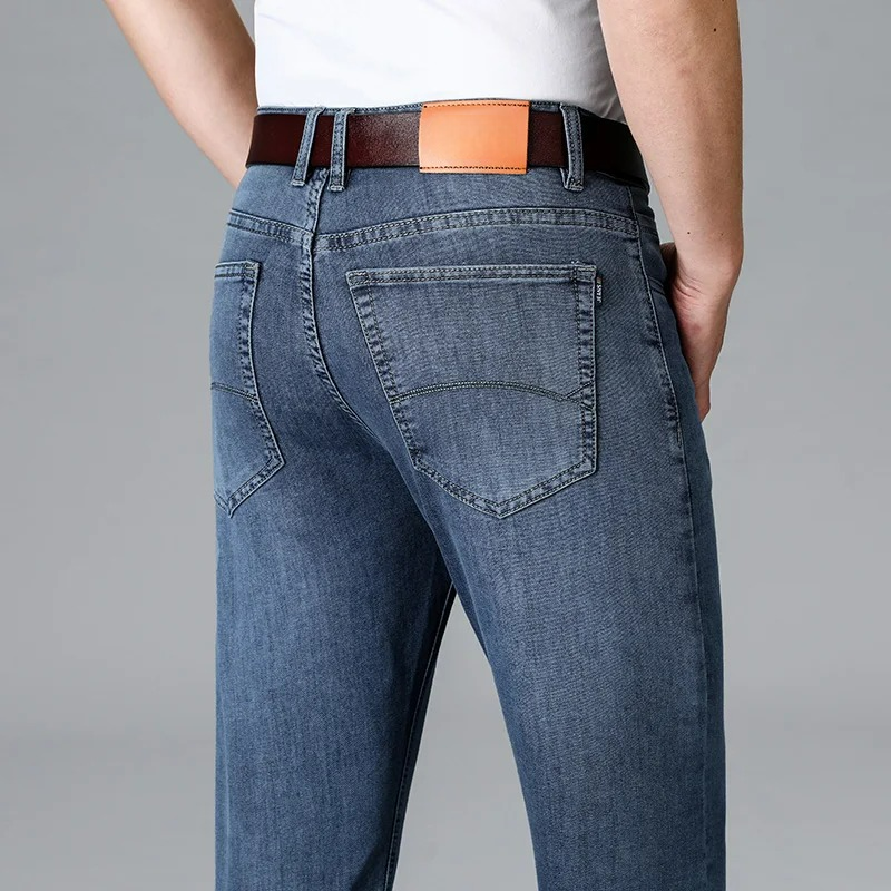 Men's stretch slim-fit light blue denim jeans rear view, showing back pockets, brown leather belt, and fitted silhouette.
