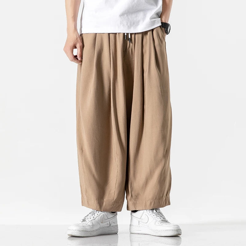 Man wearing khaki wide-leg cotton drawstring pants with white t-shirt and white sneakers on neutral background