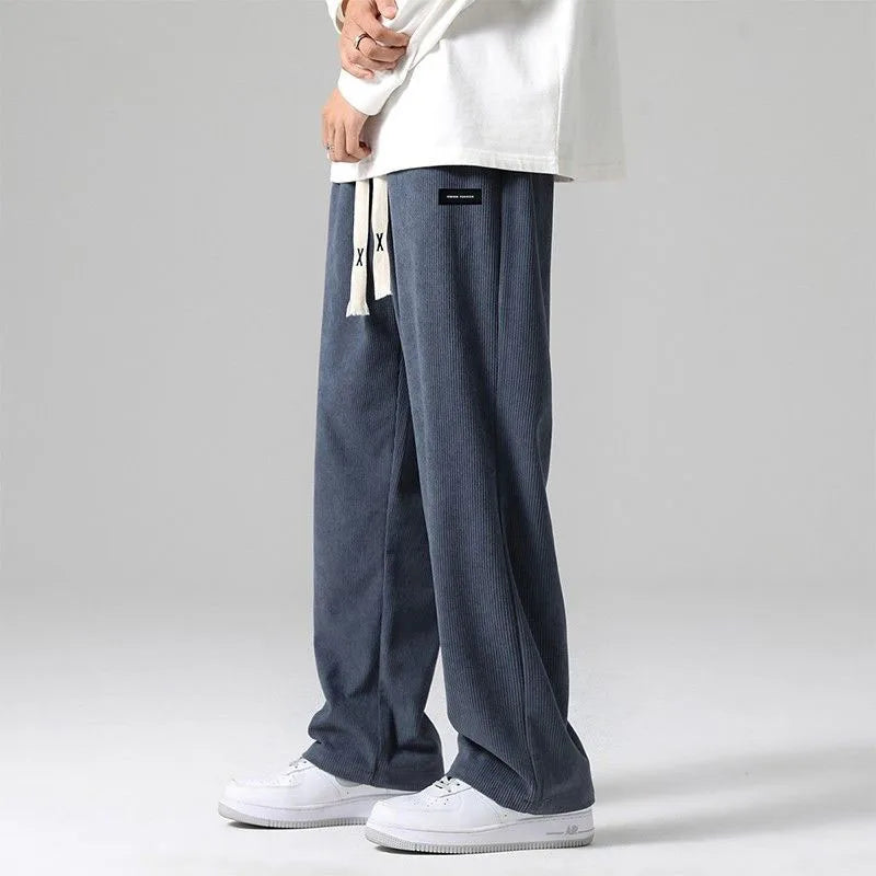 Men's blue corduroy wide-leg drawstring sweatpants with relaxed fit and elastic waistband worn with white sneakers