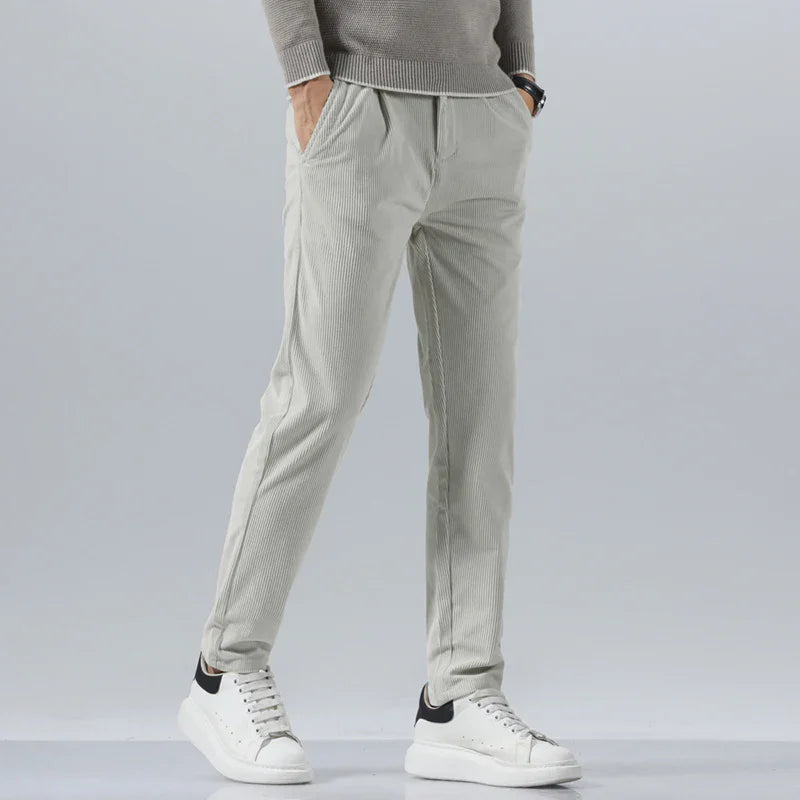 Light gray men's slim fit corduroy pants paired with a gray sweater and white sneakers, front view.