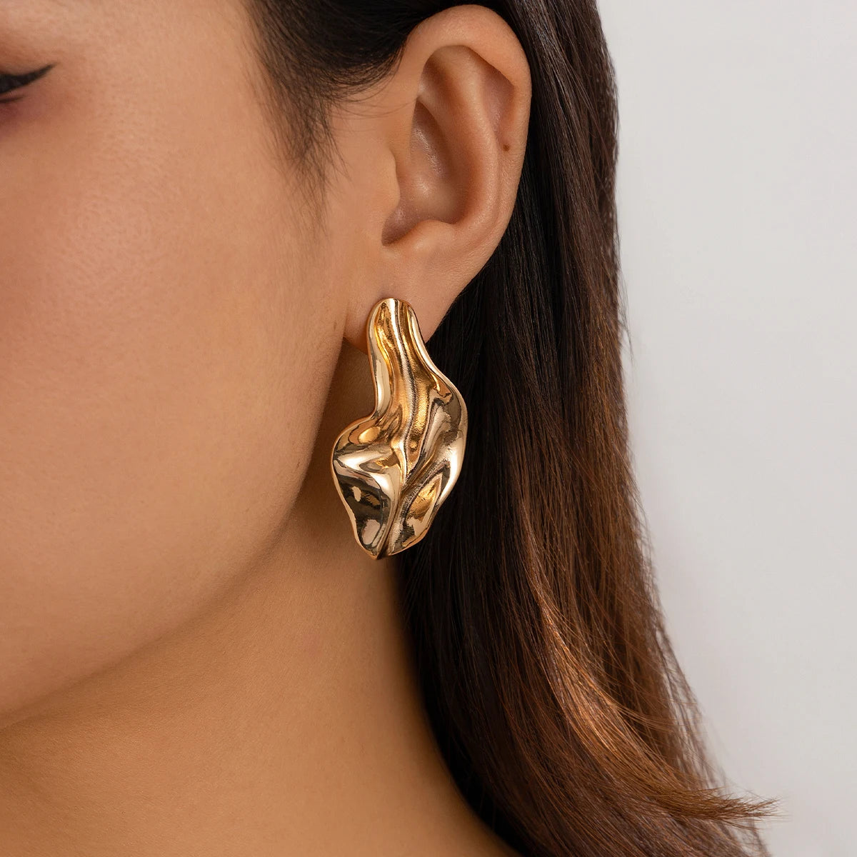 Chunky gold twisted drop earrings worn on woman's ear, statement metallic jewelry with sculptural organic shape