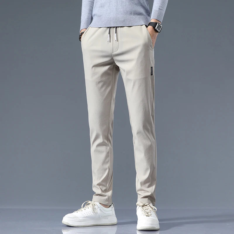 Men's beige cotton drawstring joggers with elastic waist and tapered fit, styled with gray sweater and white sneakers