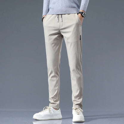 Men's beige cotton drawstring joggers with elastic waist and tapered fit, styled with gray sweater and white sneakers