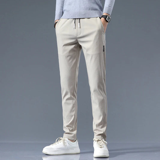Men's beige cotton drawstring joggers with elastic waist and tapered fit, styled with gray sweater and white sneakers