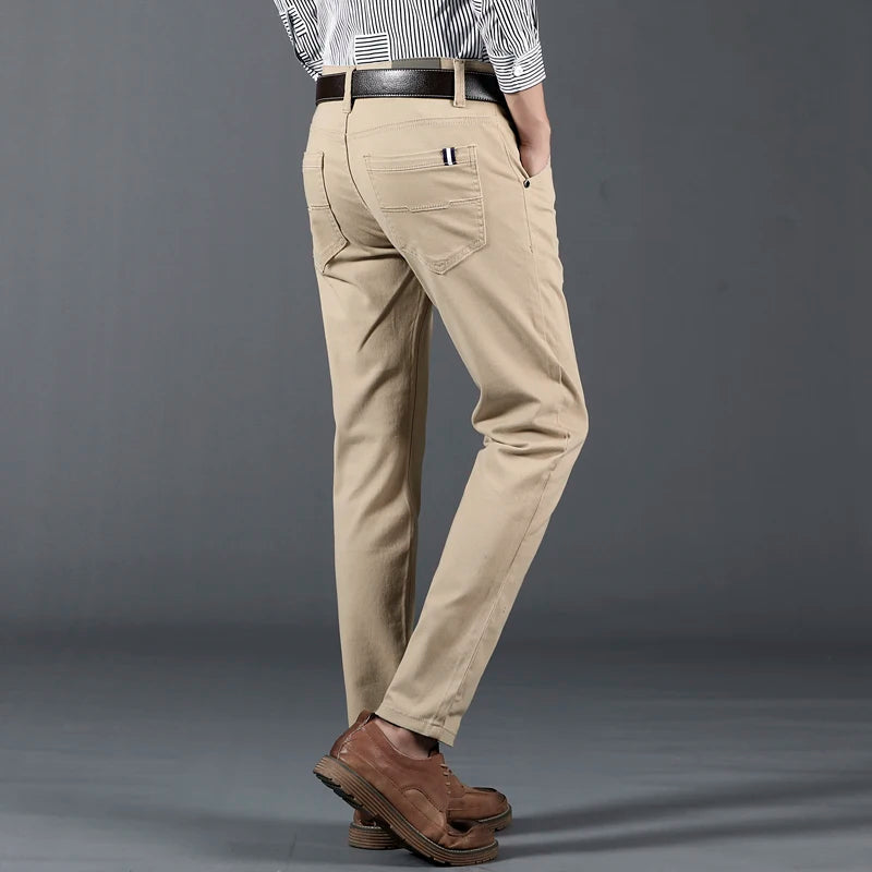 Men's slim-fit khaki cotton dress pants with brown leather belt and shoes, worn with striped shirt, back view.