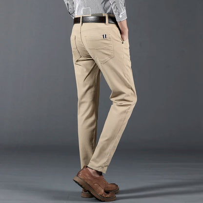 Men's slim-fit khaki cotton dress pants with brown leather belt and shoes, worn with striped shirt, back view.