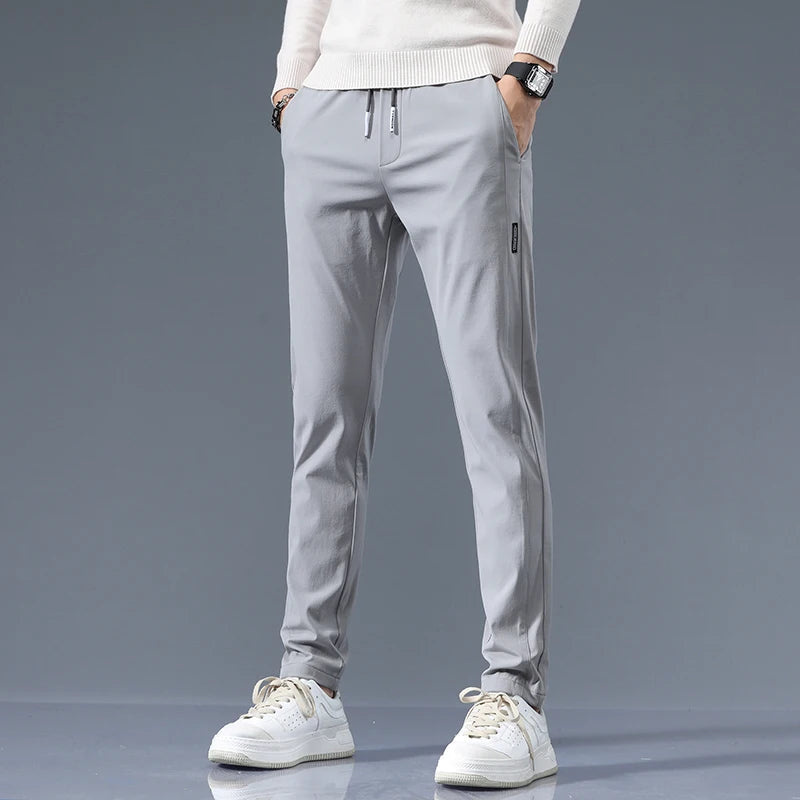 Men's light gray slim-fit cotton drawstring joggers paired with white sneakers and cream sweater on neutral background