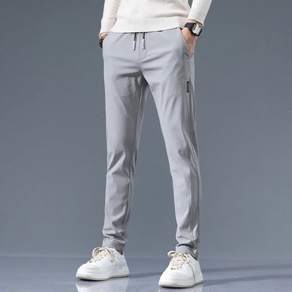 Men's light gray slim-fit cotton drawstring joggers paired with white sneakers and cream sweater on neutral background