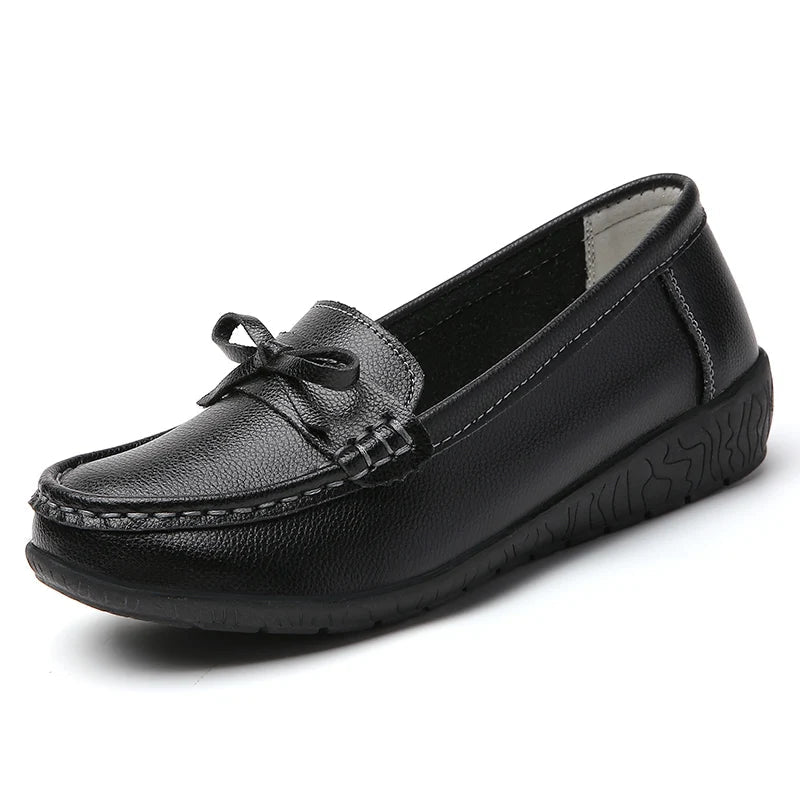 Black women's leather slip-on loafers with decorative bow detail and textured rubber sole on white background