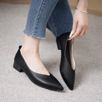 Black leather pointed-toe block heel pumps on woman wearing cropped jeans, shown being slipped on by hand.