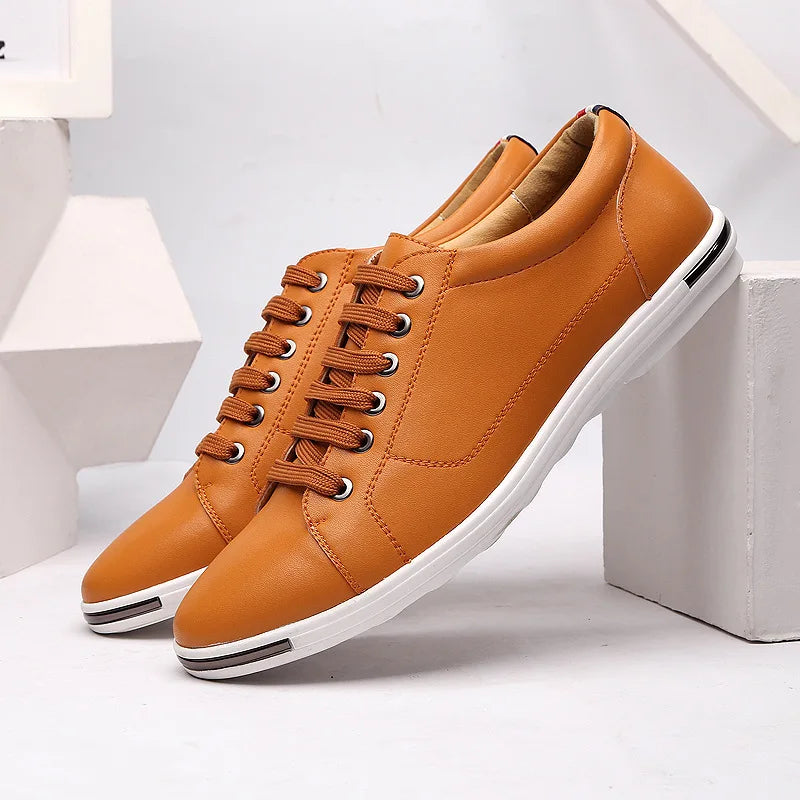 Tan leather low-top men's sneakers with matching laces, white sole, silver eyelets, and minimalist design displayed on white blocks.