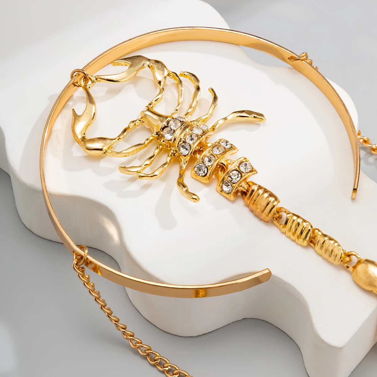 Gold scorpion upper arm cuff bracelet with crystal embellishments and chain detail displayed on white ceramic stand