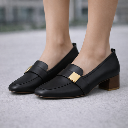 Black Italian leather block heel loafers with gold square buckle detail and orthopedic footbed, worn by a woman.