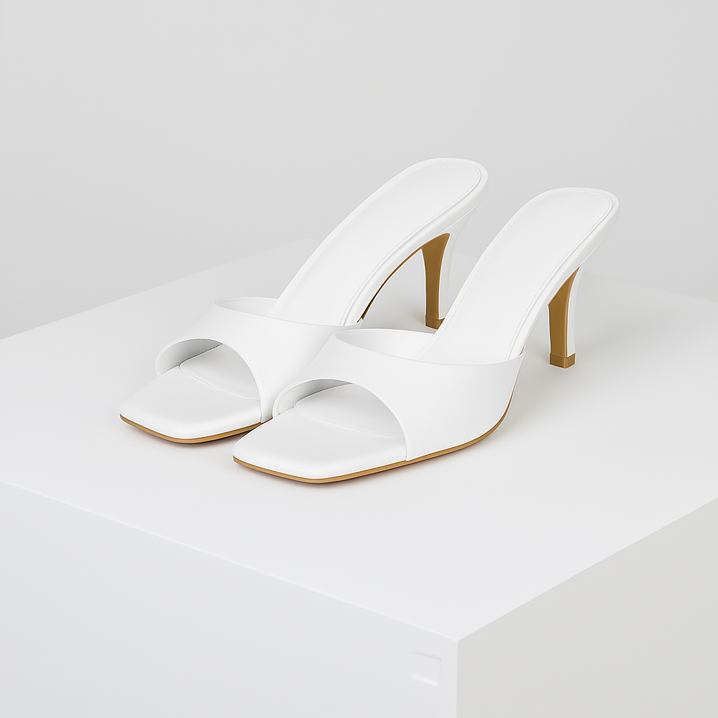 White square-toe mule heels with single strap, padded insole, and tan stiletto heel displayed on white platform