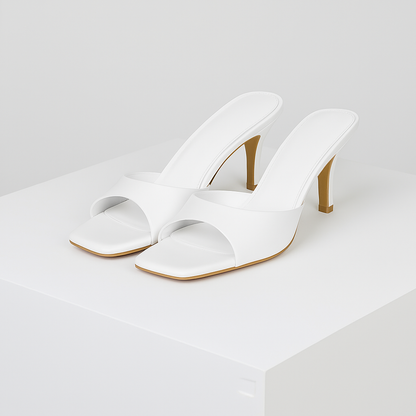 White square-toe mule heels with single strap, padded insole, and tan stiletto heel displayed on white platform